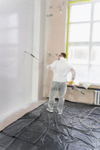 A hand holding a  paint roller, applying white paint to a textured wall. DIY painting in progress.