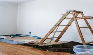 Room prepared for repainting with ladder, paint supplies, and protective floor coverings.

