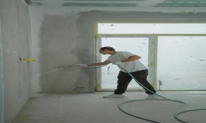 Worker spray-painting interior wall in preparation for repainting a residential space.

