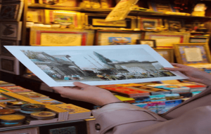 Person holding an art print in a shop filled with framed pictures and colorful books.