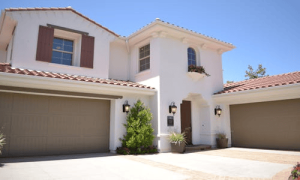 Modern suburban house with off-white walls, brown garage doors, and red-tiled roof.