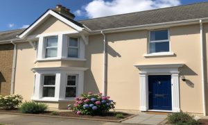 Modern house exterior with beige walls, white trim, blue front door, and colorful blooming flowers.