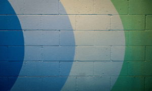 Cinder block wall featuring a painted geometric design of curved blue and green arcs.